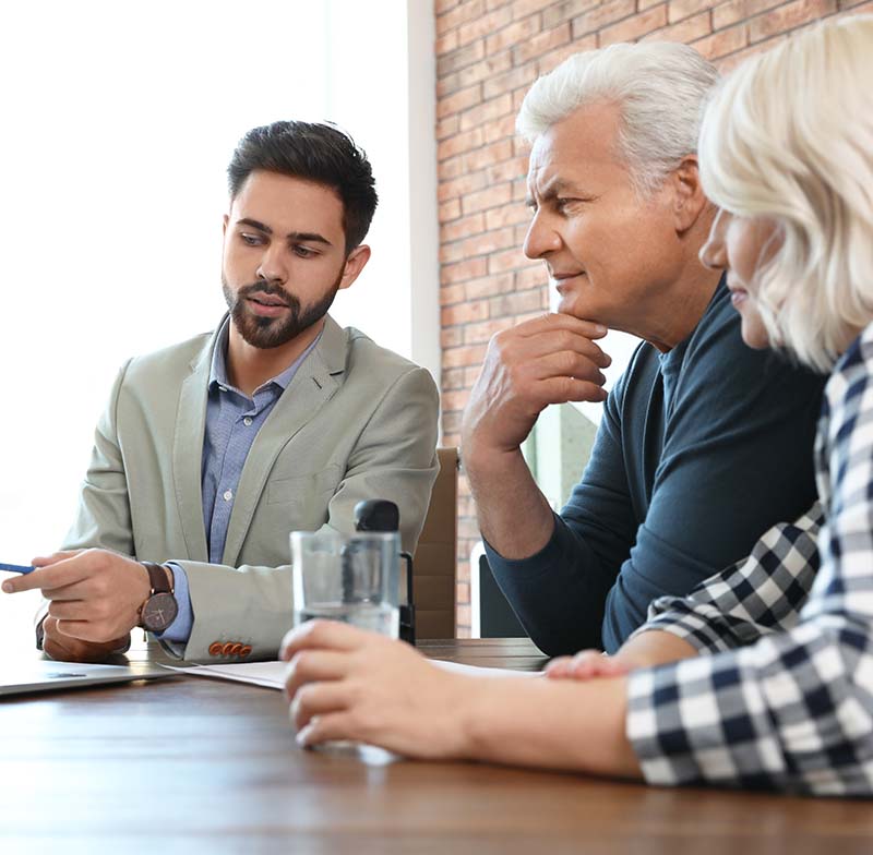 male attorney sitting with a male and female client in his office showing them something on laptop
