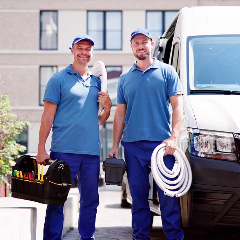 two male hvac technicians holding hvac equipment while standing next to their work van