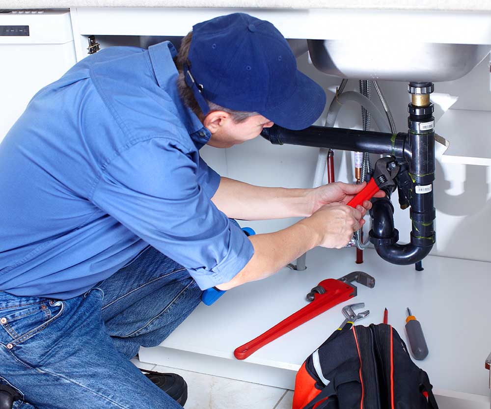 Mature plumber fixing a sink at kitchen