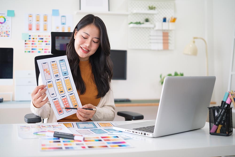 Smiling UX UI designer presenting mobile website interface prototypes during online meeting.